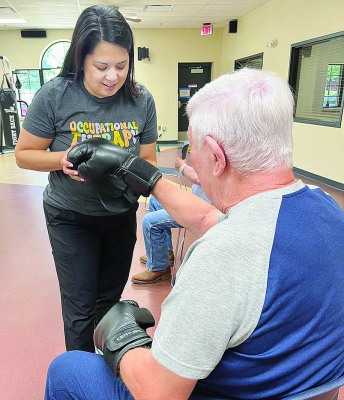 GLOVING UP -- Alicia Fritschle, COTA, helps patient with his gloves in preparation for a Rock Steady Boxing session..